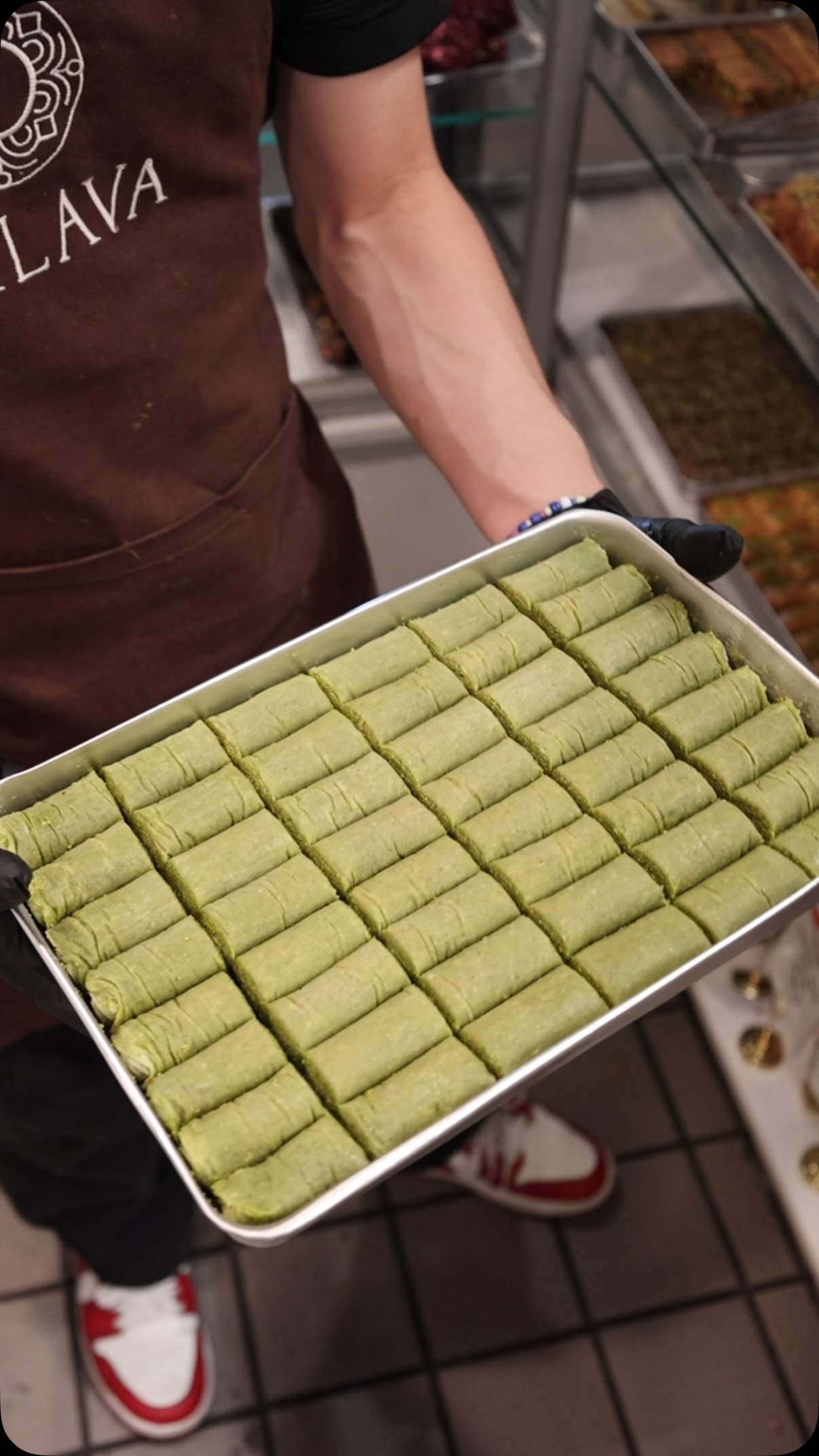 Oklava team member carrying a fresh tray of pistachio baklava