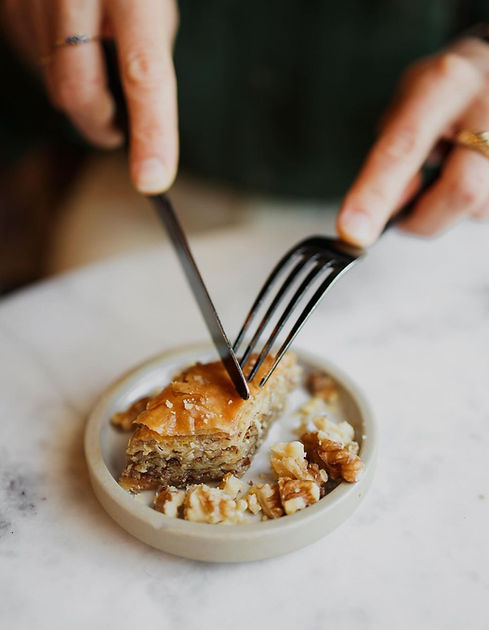 Hands cutting into a slice of baklava with a fork and knife